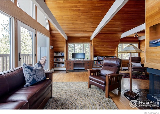 living area featuring vaulted ceiling with beams, wooden walls, wood finished floors, and a healthy amount of sunlight