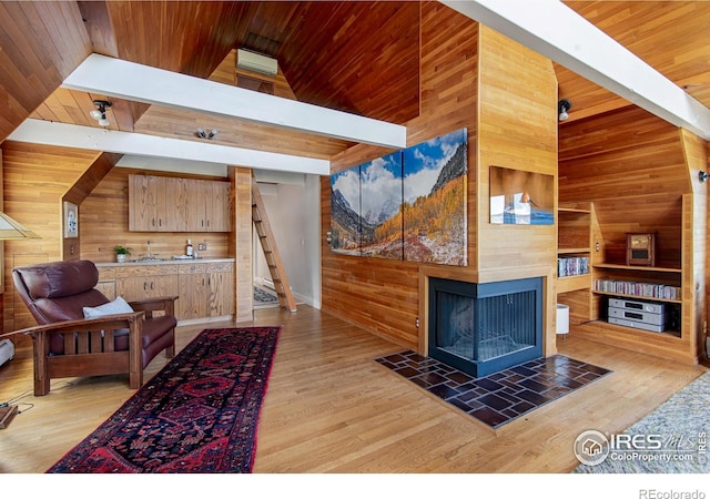 living room with wood walls, stairs, light wood-type flooring, wood ceiling, and a tiled fireplace