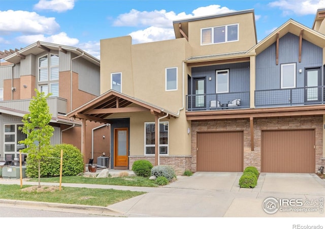 view of property featuring stone siding, a garage, stucco siding, concrete driveway, and a balcony