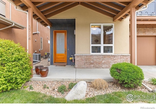 doorway to property with central AC unit, stucco siding, and stone siding
