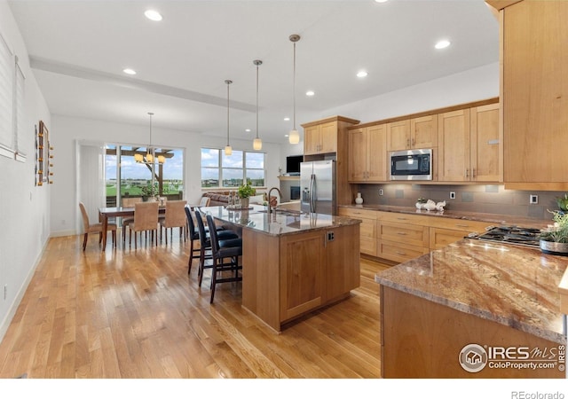 kitchen with light wood-style floors, stone counters, a kitchen breakfast bar, and stainless steel appliances