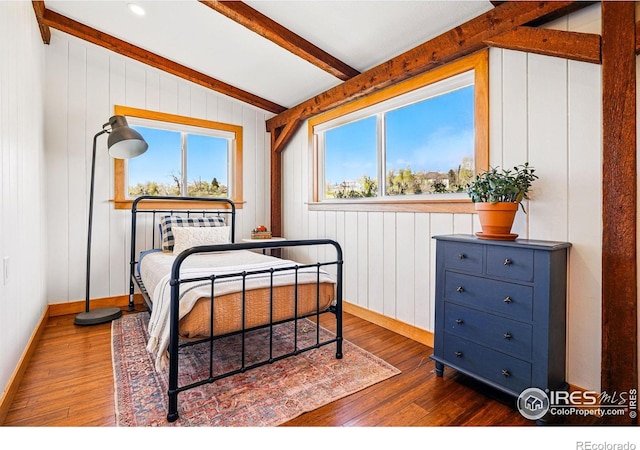 bedroom with baseboards, lofted ceiling with beams, wood walls, and dark wood-type flooring