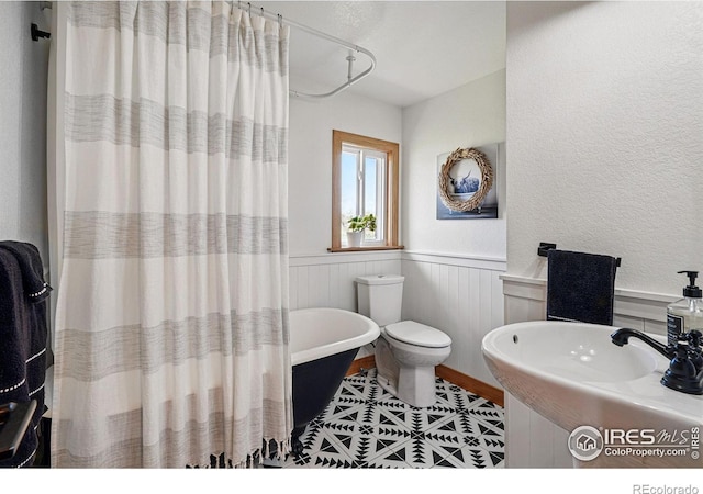 full bathroom featuring toilet, tile patterned floors, a wainscoted wall, a shower with curtain, and a soaking tub