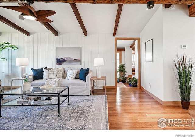 living room with a ceiling fan, beamed ceiling, baseboards, and light wood-style floors
