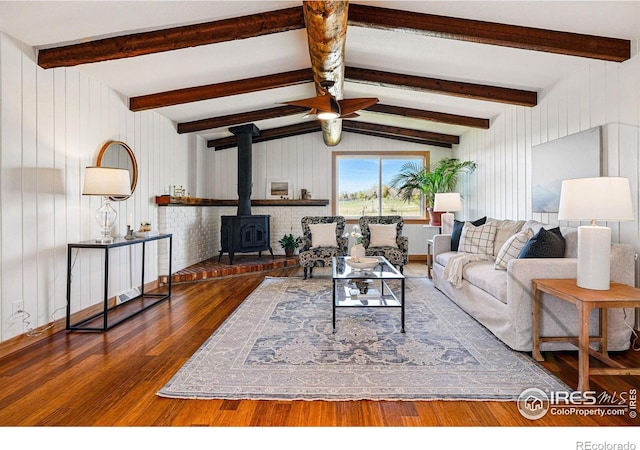 living area with vaulted ceiling with beams, a wood stove, wood walls, and wood finished floors