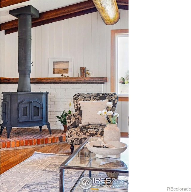 living room featuring a wood stove, wood finished floors, and beamed ceiling