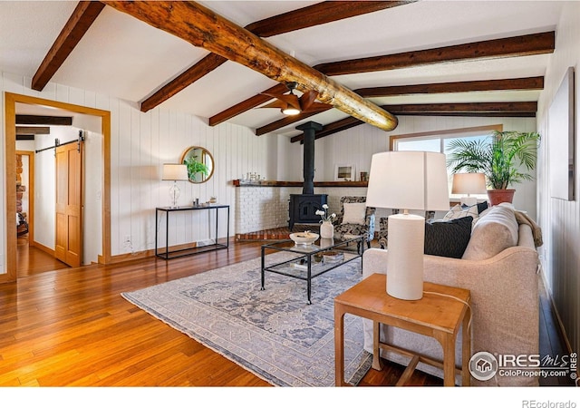 living room featuring a barn door, vaulted ceiling with beams, a wood stove, and wood finished floors
