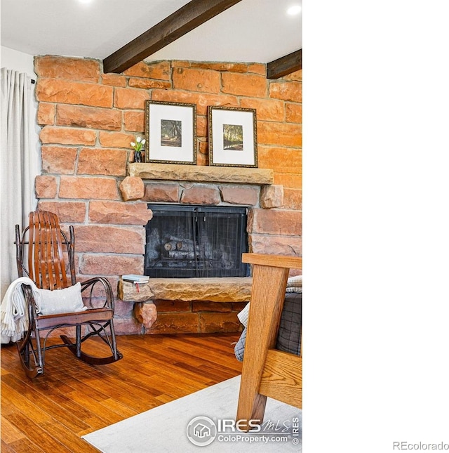 interior details with beamed ceiling, a stone fireplace, and wood finished floors