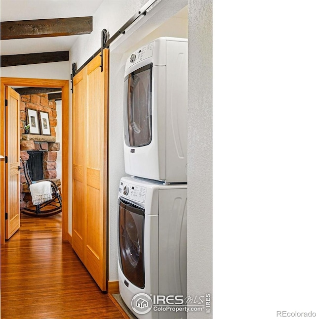 clothes washing area featuring a barn door, laundry area, stacked washer / dryer, and wood finished floors