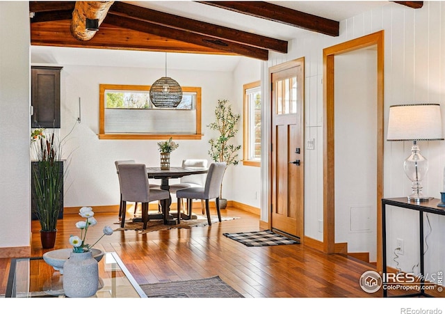 dining space featuring wood-type flooring, baseboards, and beamed ceiling