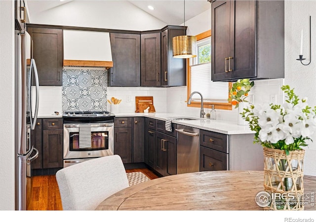 kitchen with dark brown cabinets, a sink, wall chimney exhaust hood, stainless steel appliances, and wood finished floors