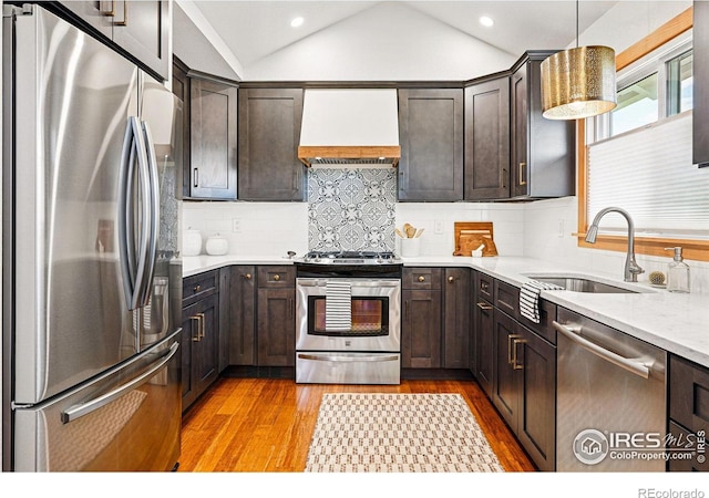 kitchen with lofted ceiling, premium range hood, a sink, light wood finished floors, and stainless steel appliances