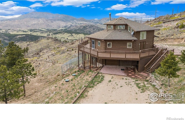 rear view of property with log siding, dirt driveway, a deck with mountain view, stairway, and a patio area