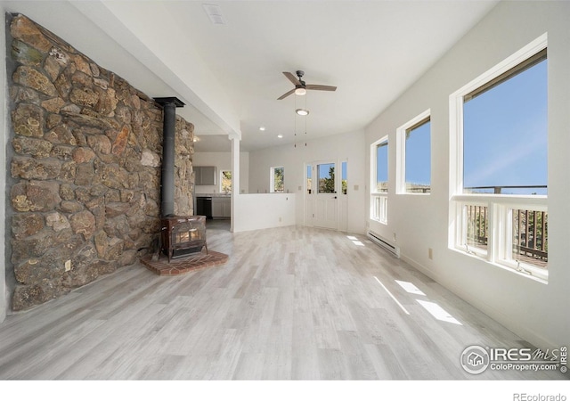 unfurnished living room with a wood stove, ceiling fan, baseboard heating, and a wealth of natural light