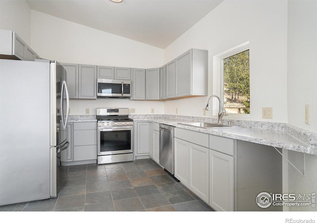 kitchen featuring light countertops, a sink, stone finish flooring, appliances with stainless steel finishes, and vaulted ceiling