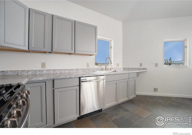 kitchen featuring appliances with stainless steel finishes, a sink, light countertops, baseboards, and gray cabinetry