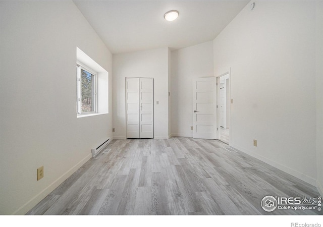 unfurnished bedroom featuring baseboards, a baseboard heating unit, light wood finished floors, and a towering ceiling