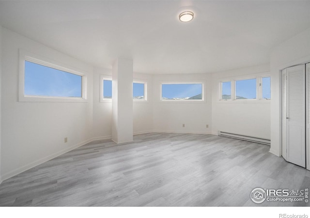 spare room featuring baseboards, baseboard heating, light wood-type flooring, and a wealth of natural light