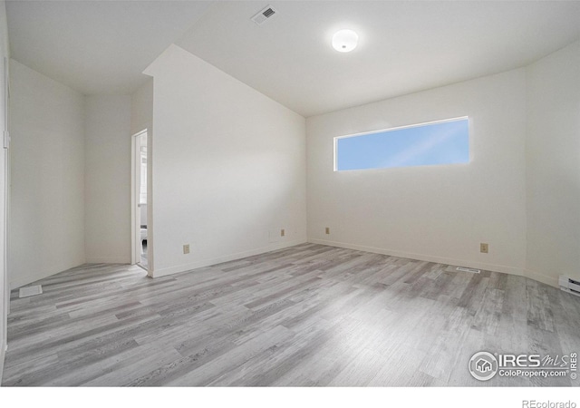 spare room featuring baseboards, vaulted ceiling, wood finished floors, and visible vents