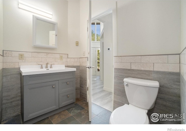 half bathroom with vanity, a wainscoted wall, toilet, and tile walls