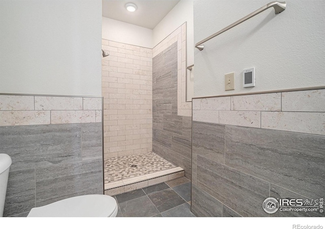 full bathroom with toilet, tile walls, a tile shower, and a wainscoted wall