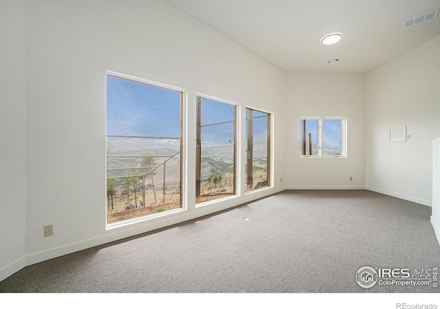 carpeted empty room featuring baseboards, a wealth of natural light, and visible vents