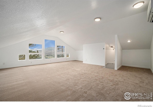 additional living space featuring carpet floors, baseboards, a wall mounted air conditioner, a textured ceiling, and vaulted ceiling
