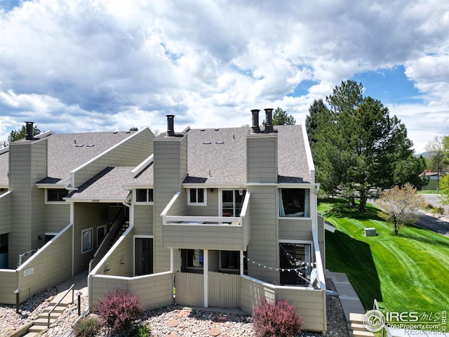 rear view of house with roof with shingles, fence, a chimney, and a yard