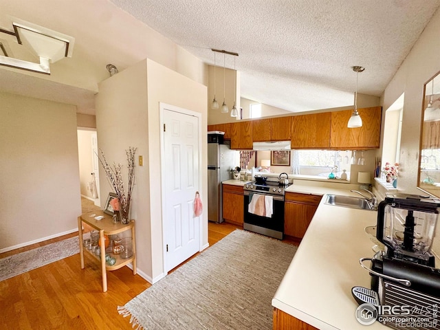 kitchen featuring a sink, brown cabinetry, stainless steel appliances, under cabinet range hood, and vaulted ceiling