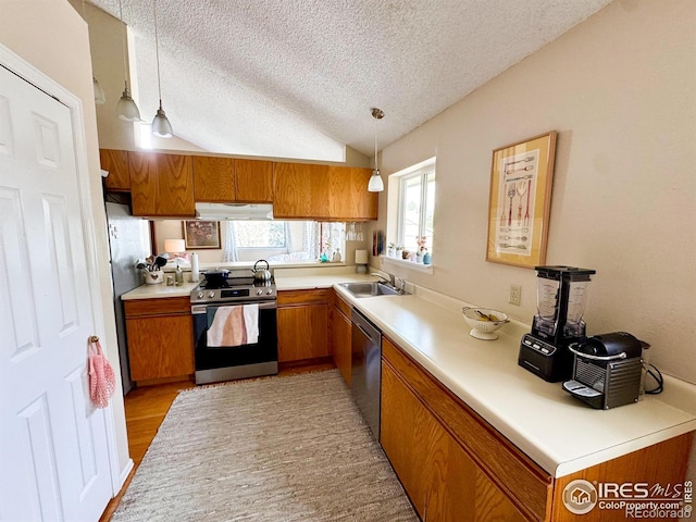 kitchen with brown cabinetry, a textured ceiling, a sink, exhaust hood, and stainless steel appliances