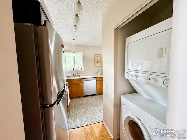 clothes washing area featuring a sink, a textured ceiling, stacked washing maching and dryer, and light wood-style flooring