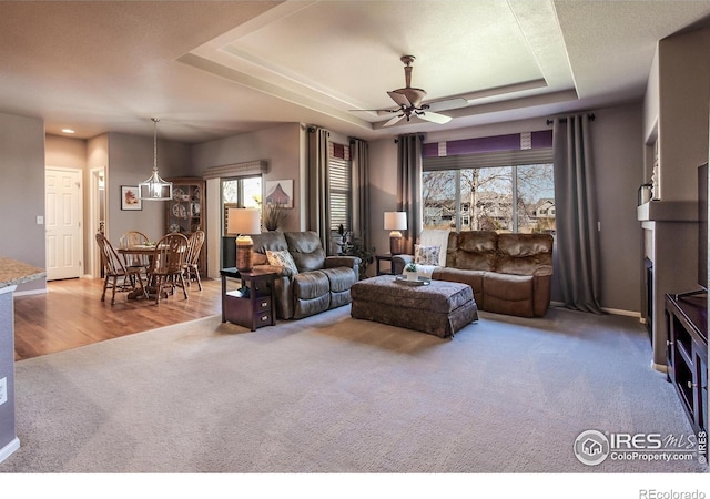 carpeted living area featuring ceiling fan, wood finished floors, a raised ceiling, baseboards, and recessed lighting