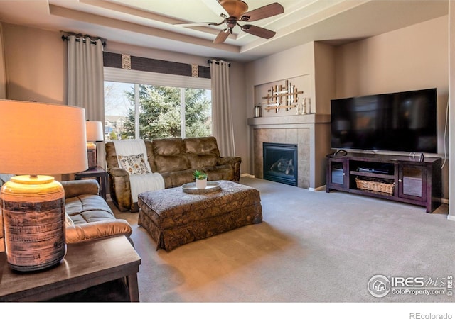 living area with a ceiling fan, a tray ceiling, carpet, and a fireplace