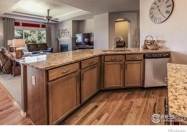 kitchen featuring a sink, arched walkways, open floor plan, stainless steel dishwasher, and a tray ceiling