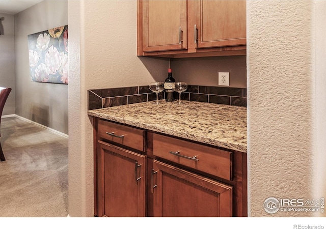 kitchen with carpet flooring, a textured wall, light stone counters, brown cabinetry, and baseboards