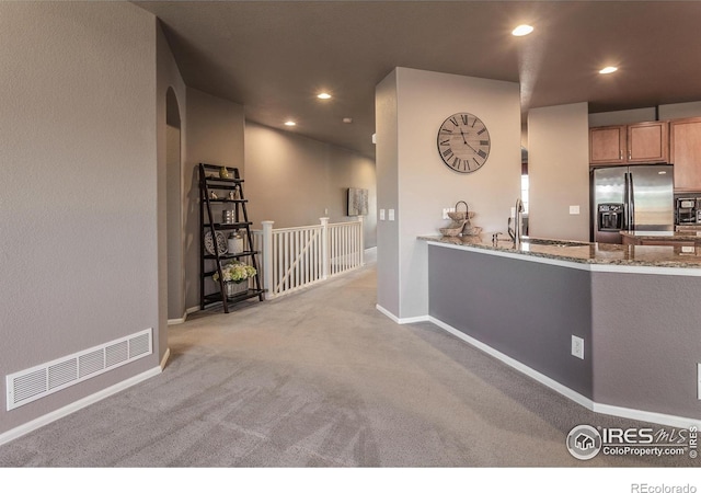kitchen featuring visible vents, stone countertops, baseboards, stainless steel refrigerator with ice dispenser, and a sink