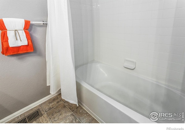 bathroom with baseboards, shower / tub combo with curtain, and visible vents