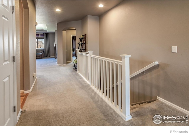 hallway featuring arched walkways, baseboards, carpet, and an upstairs landing