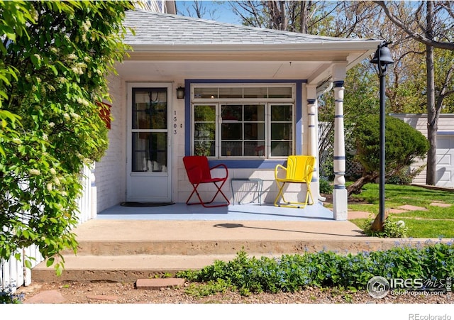 doorway to property with covered porch and a shingled roof
