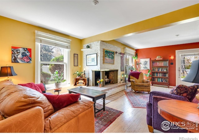 living room featuring wood-type flooring, a brick fireplace, and a healthy amount of sunlight