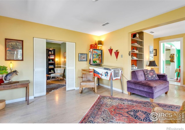 sitting room featuring built in shelves, baseboards, wood finished floors, and visible vents
