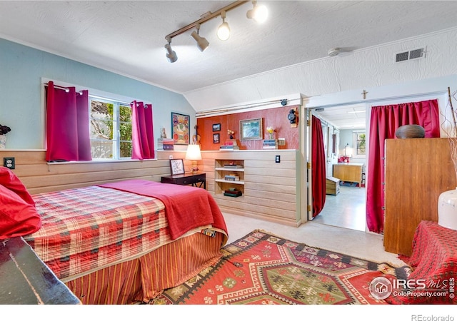 bedroom with visible vents, wood walls, rail lighting, lofted ceiling, and ornamental molding