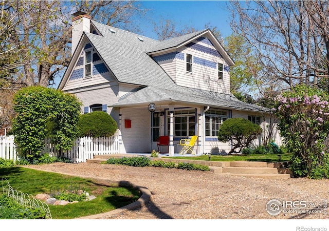 view of front of home featuring fence, covered porch, roof with shingles, a chimney, and brick siding