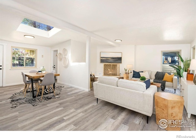 living room featuring light wood-type flooring, recessed lighting, baseboards, and a skylight