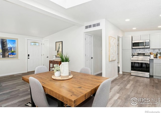 dining space with vaulted ceiling with skylight, visible vents, baseboards, light wood-style floors, and recessed lighting