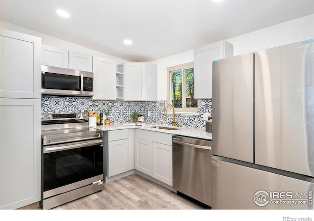 kitchen featuring decorative backsplash, appliances with stainless steel finishes, open shelves, a sink, and light wood finished floors