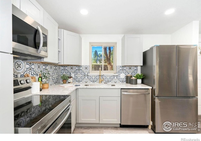 kitchen featuring decorative backsplash, appliances with stainless steel finishes, a sink, white cabinets, and light wood finished floors