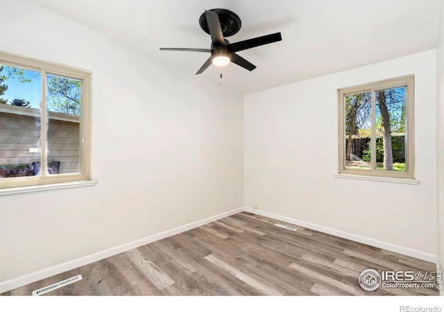 empty room with baseboards, visible vents, plenty of natural light, and wood finished floors