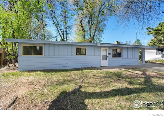 ranch-style home featuring board and batten siding, a chimney, and a front lawn
