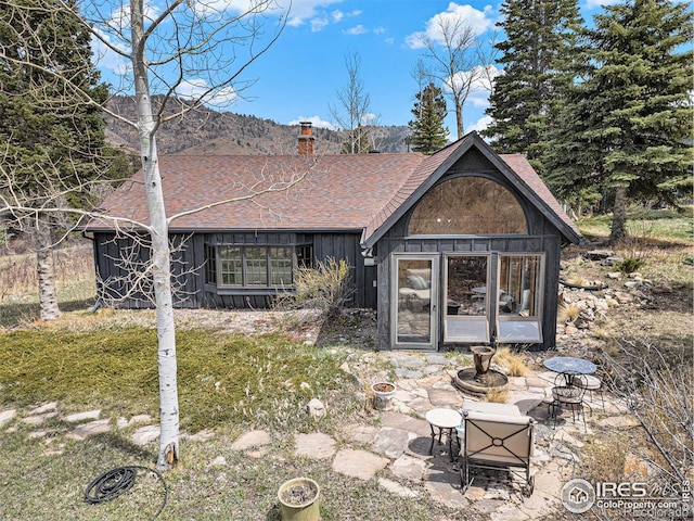 back of property with a chimney, board and batten siding, a shingled roof, and a patio